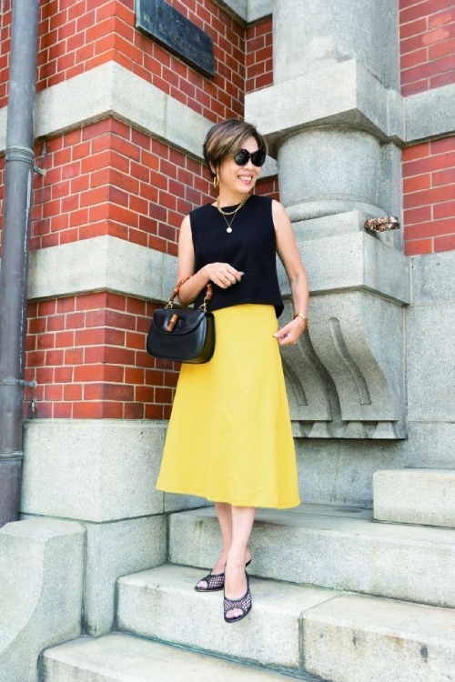 裙子剛好遮住較粗壯的小腿肚，是最能展現纖細感的長度，黑色上衣、黃色裙子和黑色手提包、金色項鍊相呼應，是提升時尚感的小技巧。（出自《アンダー153cm、60歳。カッコよく着こなす大人コーデ》）