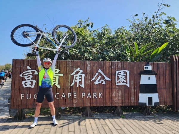 林至芃參加台大EMBA單車隊，在富貴角公園前舉起單車拍照。