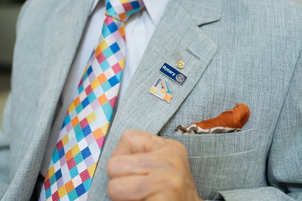 侯登見身著西裝，搭配扶輪社領帶和徽章。 