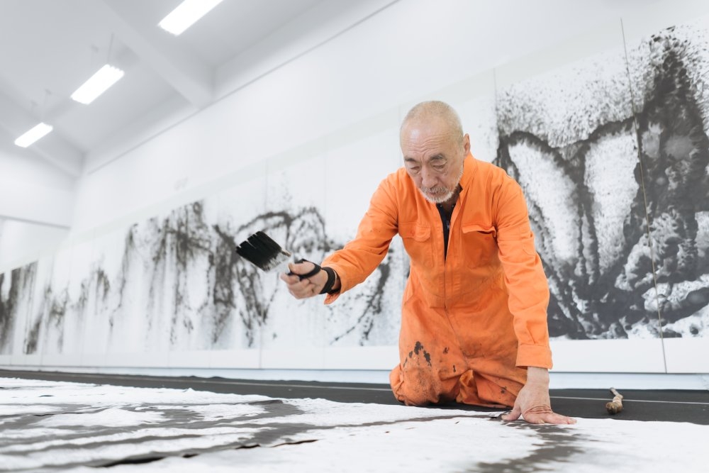 程延平右手拿刷子，左手撐住身體，跪趴在地創作當代水墨。