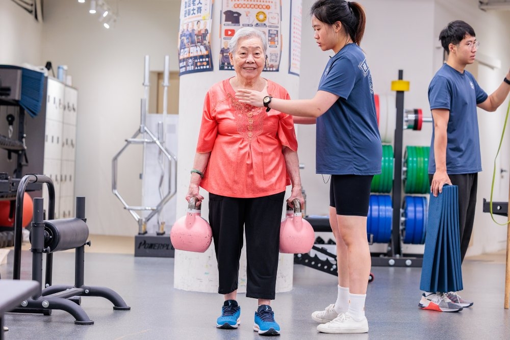 在教練指導下，鄭陳金梅手持單邊8公斤重的啞鈴負重行走，增加身體穩定度。