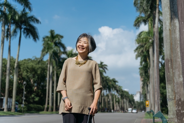 即使左手拄著拐杖，沐浴在台大椰林大道上的陽光下，宋玫玫仍笑得燦爛。（圖片來源：影巷26號攝）